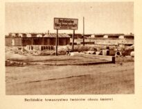 Tablica berlińskiego przedsiębiorstwa budowlanego, umieszczona przy pierwszym wjeździe do obozu (od strony Piask). W głębi po prawej barak firmy budowlanej, za nim baraki komendantury. Z prawej położona na grobli droga prowadząca w głąb obozu. Za nią baraki Wachbataillonu.