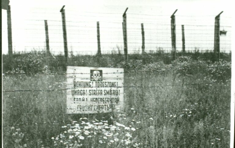 Tablica ostrzegawcza o treści "UWAGA! STREFA ŚMIERCI" na jednym z pól więźniarskich. Tekst powtórzony w języku niemieckim, polskim i rosyjskim.
